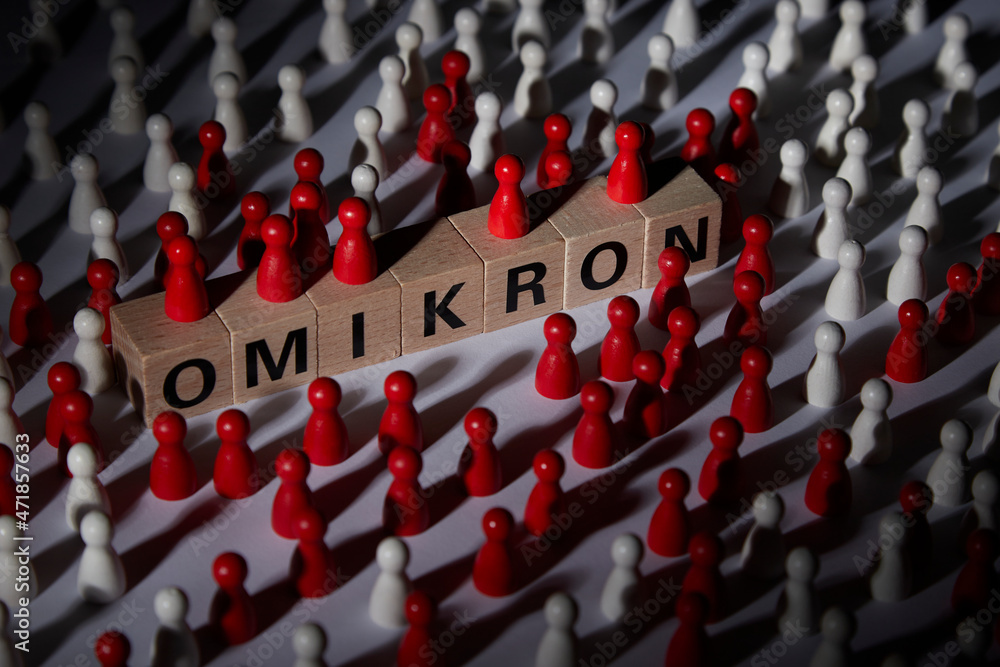 Fototapeta premium wooden blocks with the word omicron surrounded by wooden figurines as symbol for covid-19 crisis