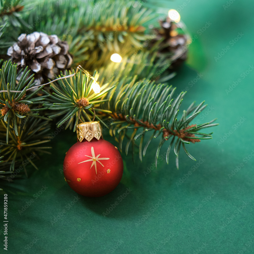 Christmas red ball, Christmas tree, cones and garland with lights on green background. Concept: Christmas and New Year, winter holiday theme. Selective focus. Square. Christmas red ball, Christmas tree, cones and garland with lights on green background. Concept: Christmas and New Year, winter holiday theme. Selective focus. Square.