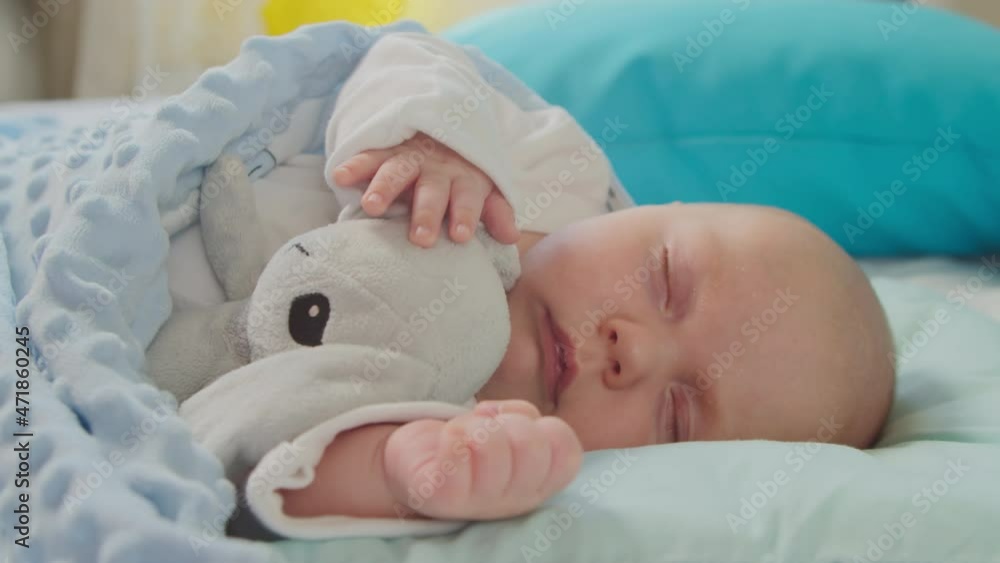 Sleeping baby in a crib hugs a toy in his sleep. Newborn baby sleeps on a bed in a room. Concept