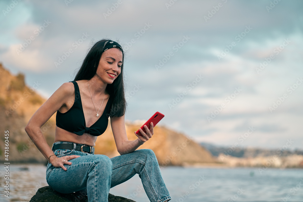 Woman young looking at smartphone sitting on a beach rock