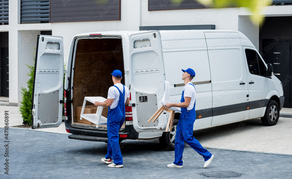 Two removal company workers are loading boxes and furniture into a minibus. Two removal company workers are loading boxes and furniture into a minibus.
