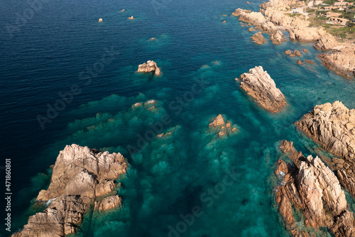 Aerial top down shot of a stone shoreline and turquoise sea water illuminated by the sun.