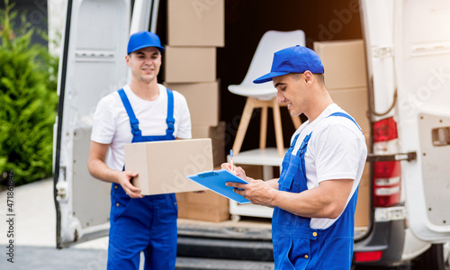 Two removal company workers unloading boxes from minibus into new home