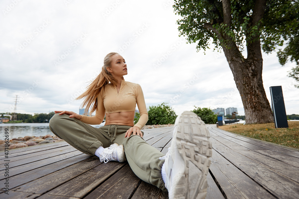 Blonde young athletic woman working out in a park in an urban environment. Attractive athletic woman exercising outdoors in the morning, copy space. Health, fitness concept