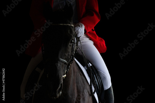 A rider in red jacket on horseback riding on dark background. Sportsman on black horse isolated on black background.