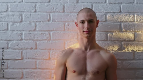 Sunrays on a Handsome bald shirtless adult gay man posing in font of white wall. . High quality 4k footage