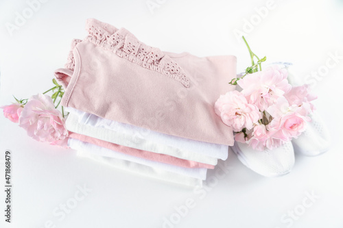 A stack of pink and white beachwear for children on a white background. Sneakers decorated with pink flowers