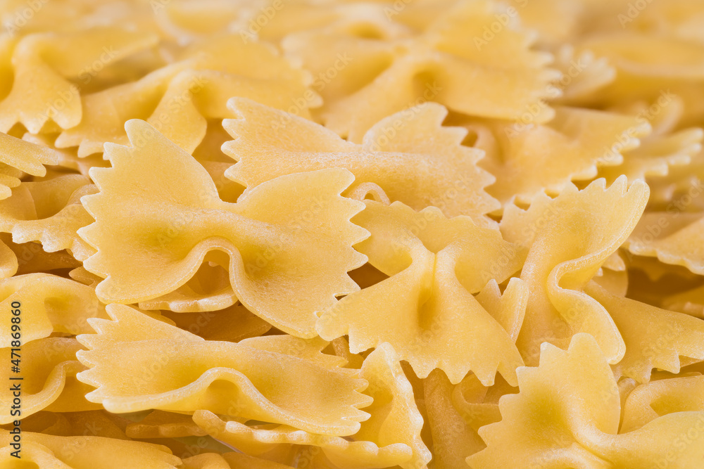 Detail of raw egg butterfly pastas on heap with beautiful blurring in background. Closeup of yellow bow-tie pasta texture. Uncooked dry farfalle with scalloped edge. Italian staple food. Healthy diet.