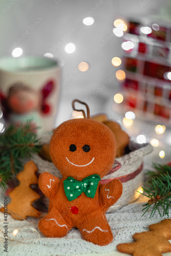 A Christmas gingerbred man sits near a basket of ginger cookies on a blurred background. Christmas soft tree toy.