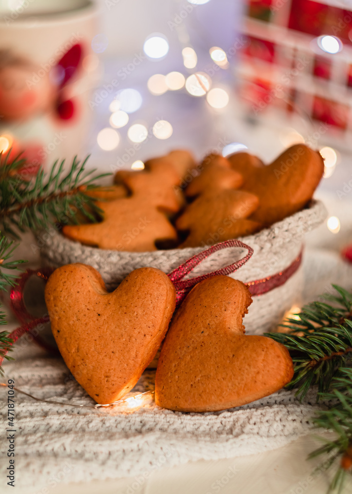 Heart shaped Christmas gingerbread cookies in a knitted basket near fir tree branches on a blurred background. Homemade Christmas cookies. Heart shaped Christmas gingerbread cookies in a knitted basket near fir tree branches on a blurred background. Homemade Christmas cookies.