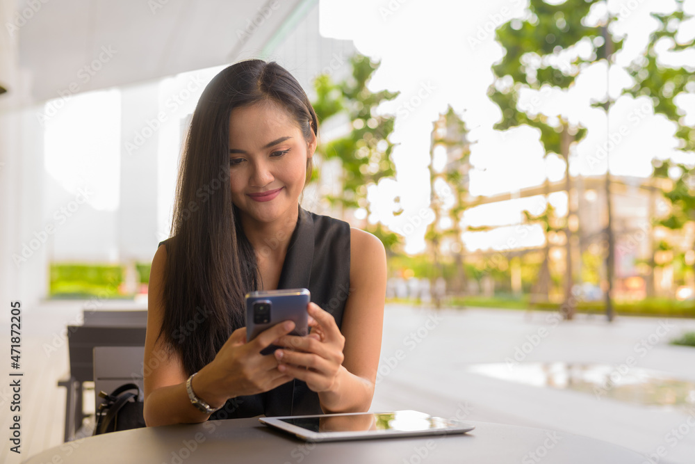 Portrait of beautiful Asian woman sitting outdoors at coffee shop restaurant using mobile phone Portrait of beautiful Asian woman sitting outdoors at coffee shop restaurant using mobile phone