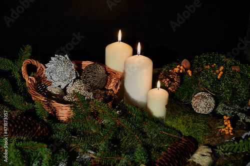 Christmas balls in the basket. Candles. Spruce branch, green moss, yellow forest berries, hazelnuts, cones, birch bark.