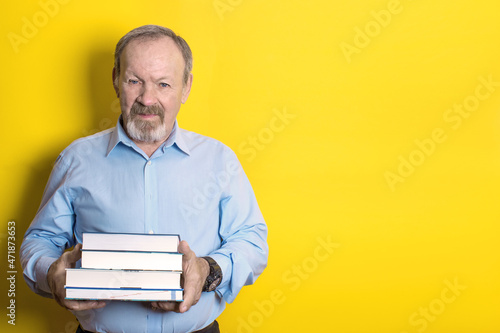 smiling elderly man holding a stack of books in his hands on a yellow background. copy space