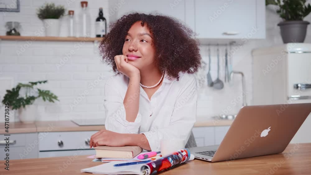Carried away woman African American sits at table and smiling. Joyful Hispanic female in cozy kitchen, dreaming of future success. Thinking about future or positive memories, lifestyle Carried away woman African American sits at table and smiling. Joyful Hispanic female in cozy kitchen, dreaming of future success. Thinking about future or positive memories, lifestyle
