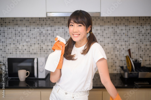 Young beautiful woman wearing protective rubber gloves is cleaning table in kitchen at home.