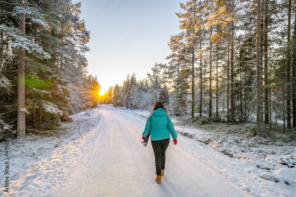 A calm tranquil view of the snow covered trees in the snowdrifts and beautiful sunset. A beautiful woman in coloured jacket walking through the Magical winter forest.