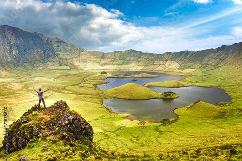 The landscape of Corvo Island in the Azores with man on rock peak with open arms. Concept of freedom and travel adventure. photo
