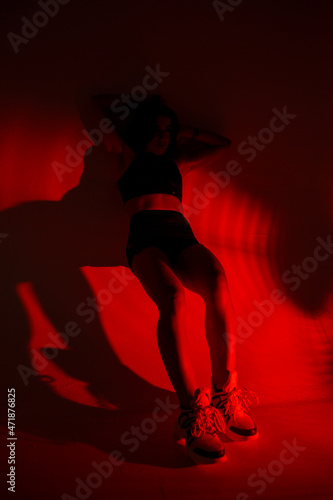 Photoshoot of a young brunette in a photo studio. Beautiful slender woman in a black top and shorts in red light.