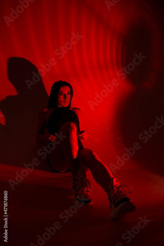 Photoshoot of a young brunette in a photo studio. Beautiful slender woman in a black top and shorts in red light.