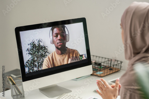 Young African student on computer screen looking at his teacher in hijab explaining him some points of online lesson