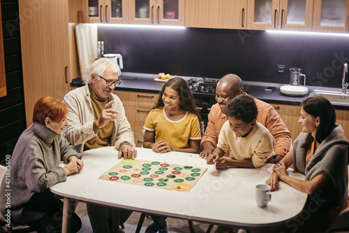 Large happy multiracial family of three generations playing board game while sitting by table in the kitchen