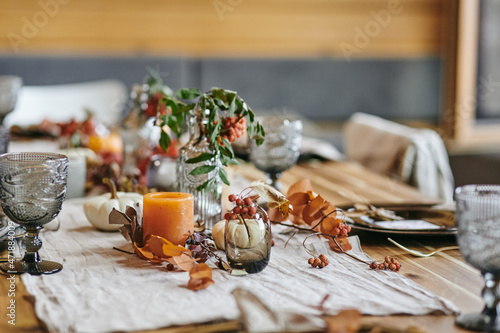 Still life of autumn leaves in vase and bottle on festive table served with glasses and kitchenware for family dinner