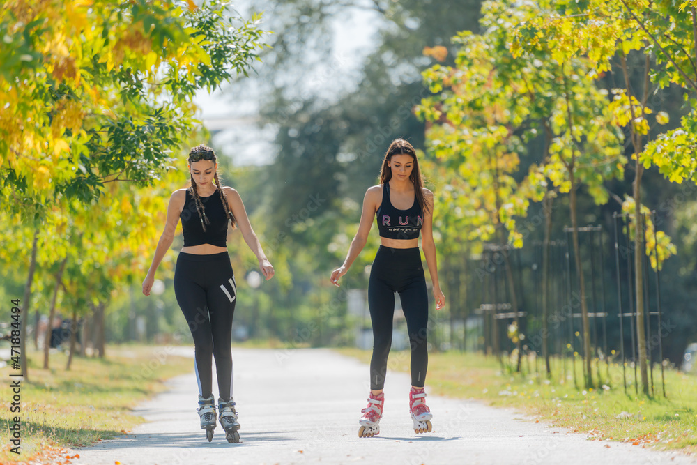 Obraz premium Full body portrait of happy sportswomen rollerskating in the park on a sunny day