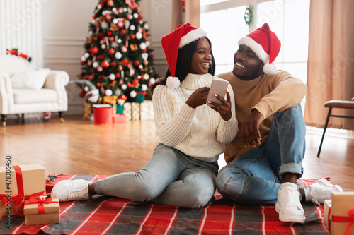 Happy festive black family using cellphone choosing gifts on Xmas photo