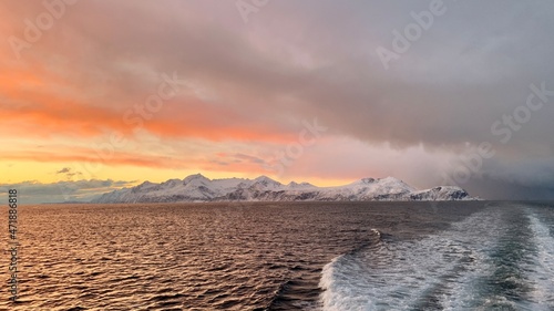 Arktische Reise auf einem Boot oder Schiff im Winter im Norden Norwegens in einem Fjord mit schneebedeckten Bergen und einem pastellfarbenem Himmel