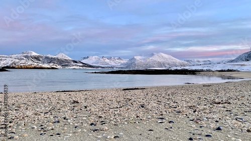 Arktische Reise auf einem Boot oder Schiff im Winter im Norden Norwegens in einem Fjord mit schneebedeckten Bergen und einem pastellfarbenem Himmel