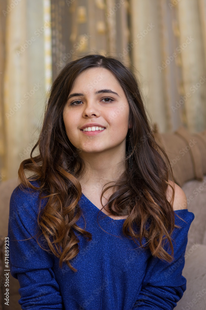 Young smiling beautiful girl with long hair sits on a soft sofa in a cozy home Young smiling beautiful girl with long hair sits on a soft sofa in a cozy home