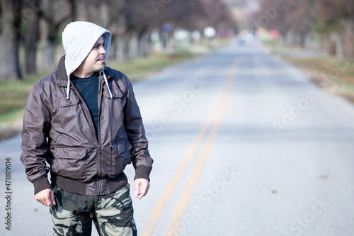 Cool guy looking outdoors in an empty street with a brown jacket and camo pants. © Carlos Morales