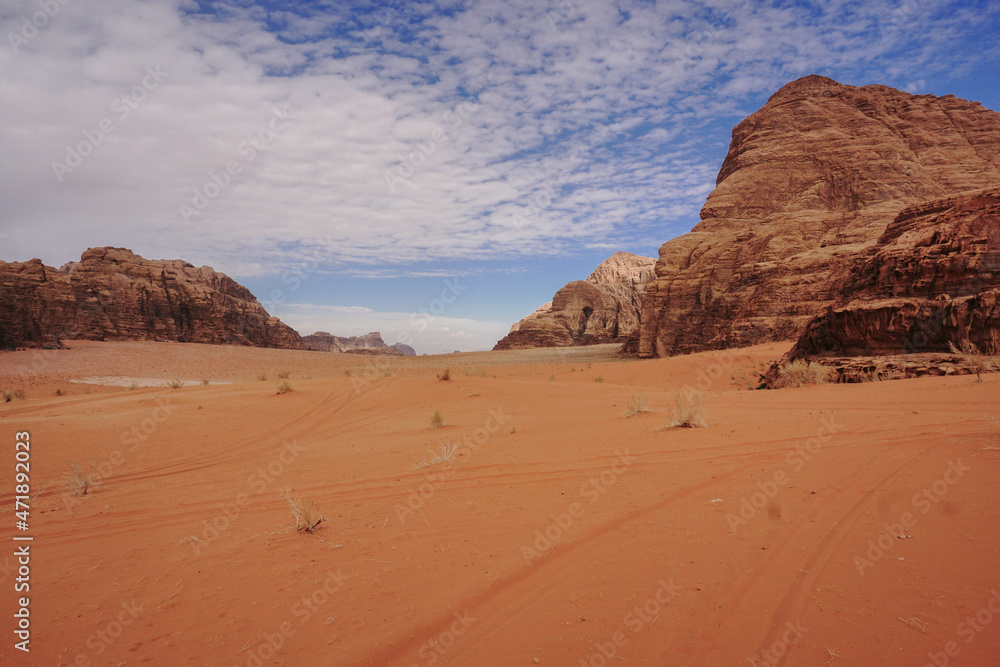 red valley in the Wadi Rum desert, beautiful weathered mountains around, rich blue sky with beautiful clouds, car tracks in the sand, nature of Jordan