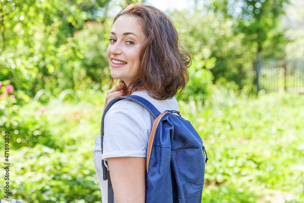 Happy positive student girl with backpack smiling on green park background. Woman having rest in campus during lunch break. Education and leisure concept Happy positive student girl with backpack smiling on green park background. Woman having rest in campus during lunch break. Education and leisure concept