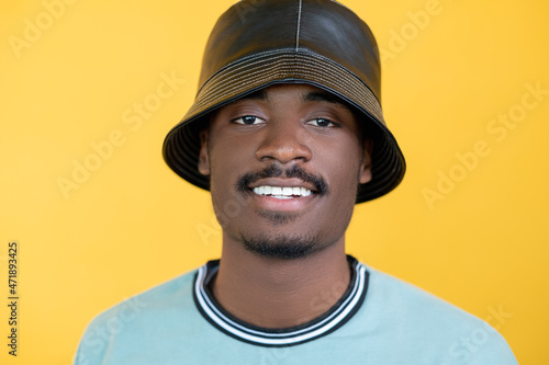 Rapper man. Urban style. Model shooting. Happy hipster guy in sweatshirt and leather hat isolated yellow background. © golubovy