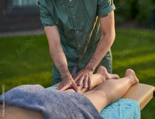 Male therapist giving foot massage massage to athlete patient on bed in beautiful yard for sports physical therapy concept. selective focus