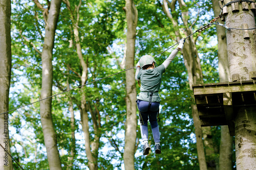 School boy in forest adventure park. Acitve child, kid in helmet climbs on high rope trail. Agility skills and climbing outdoor amusement center for children. Outdoors activity for kid and families.