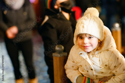 Cute little preschool girl on winter evening on christmas market. Happy smiling child in warm clothes. Joyful kid portrait