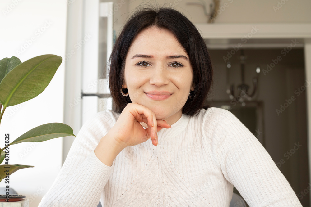Shot of a screen of young woman doing a virtual conference from her home office. Looking at camera webcam and smiling