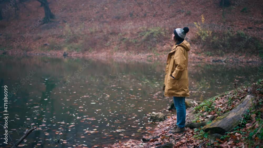 A woman in a long jacket and hat stands on the shore of a forest lake and enjoys the view on a foggy autumn day. A woman in a long jacket and hat stands on the shore of a forest lake and enjoys the view on a foggy autumn day.
