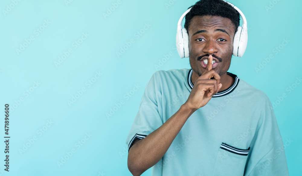 Hush gesture. Secret man. Best sound. Hipster guy in white headphones holding finger on lips isolated blue copy space. Hush gesture. Secret man. Best sound. Hipster guy in white headphones holding finger on lips isolated blue copy space.