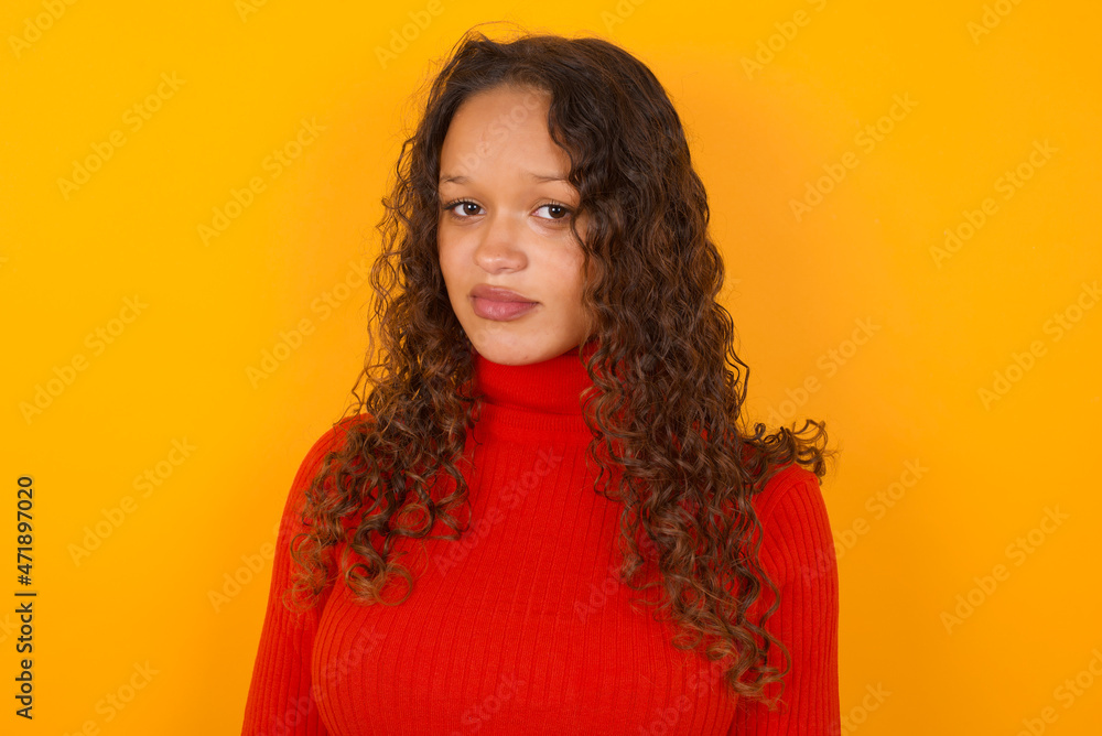 Teenager girl with curly hair wearing red sweater over yellow background crying desperate and depressed with tears on his eyes suffering pain and depression. Sad facial expression and emotion concept. Teenager girl with curly hair wearing red sweater over yellow background crying desperate and depressed with tears on his eyes suffering pain and depression. Sad facial expression and emotion concept.