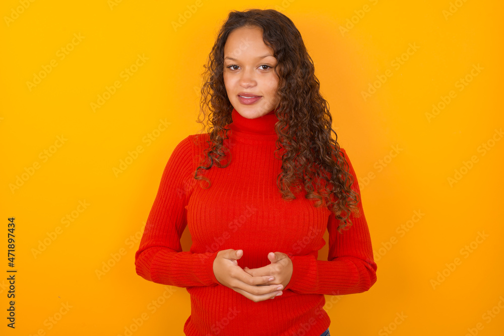 Business Concept - Portrait of teenager girl wearing red knitted sweater against yellow background holding hands with confident face. Business Concept - Portrait of teenager girl wearing red knitted sweater against yellow background holding hands with confident face.
