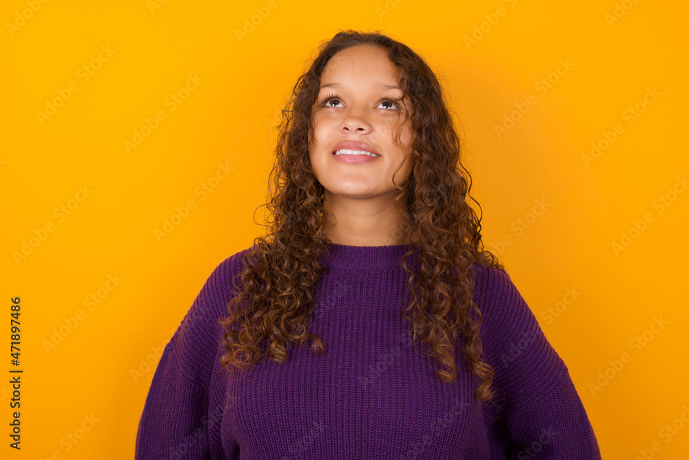 Surprised teenager girl wearing purple knitted sweater against yellow background , shrugs shoulders, looking sideways, being happy and excited. Sudden reactions concept. Surprised teenager girl wearing purple knitted sweater against yellow background , shrugs shoulders, looking sideways, being happy and excited. Sudden reactions concept.
