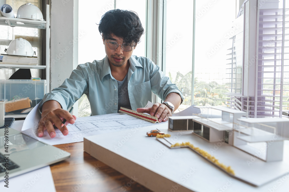 Asian men messy hair Speed up working architecture or Interior Designer study about building design with drawing paper, Building model on desk in bright home office. Technology for design freelance. Asian men messy hair Speed up working architecture or Interior Designer study about building design with drawing paper, Building model on desk in bright home office. Technology for design freelance.