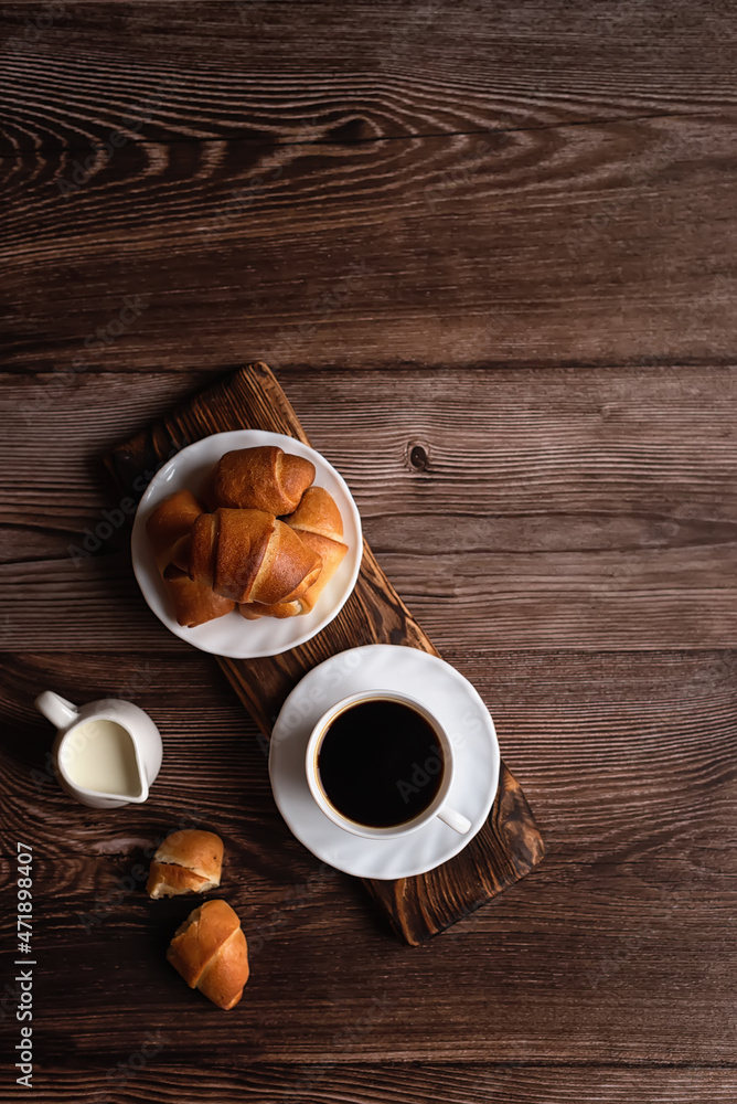A cup of coffee and croissants on a dark wooden background. Free space for signature. A cup of coffee and croissants on a dark wooden background. Free space for signature.