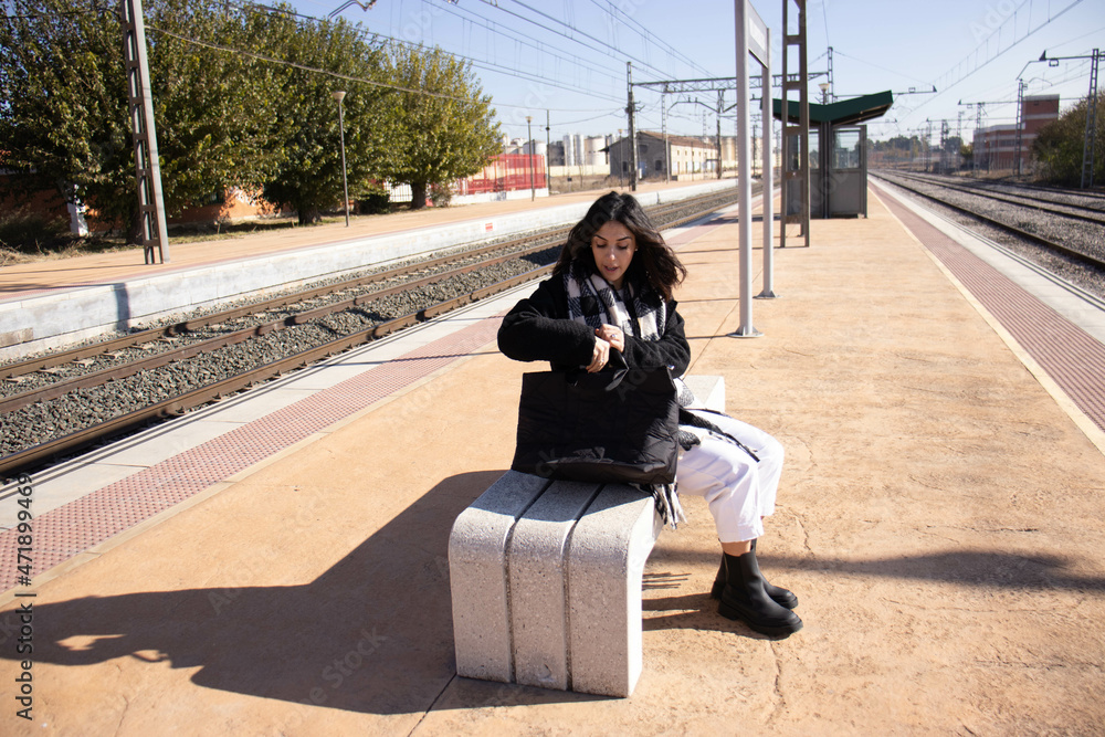 Fototapeta premium young brunette woman next to railroad arden with luggage, waiting for passenger train.