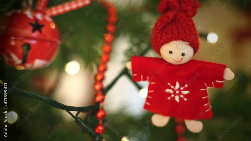 woolen handmade doll with red knit hat on Christmas tree among decorations and string lights woolen handmade doll with red knit hat on Christmas tree among decorations and string lights