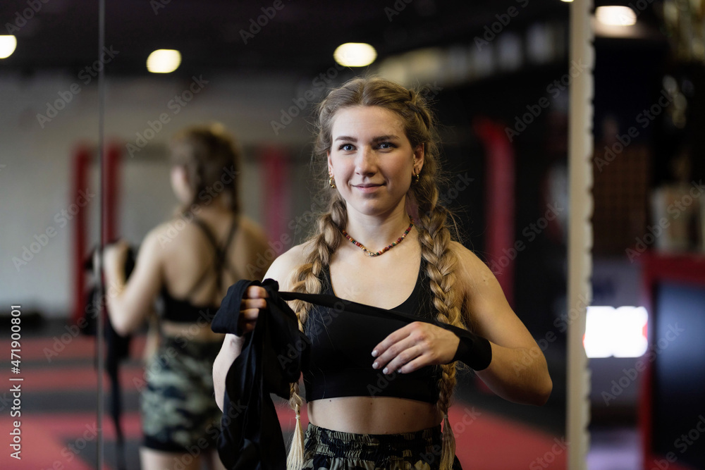 A young smiling woman with braids prepares for a workout, she wraps a tight bandage around her hands to protect them. 