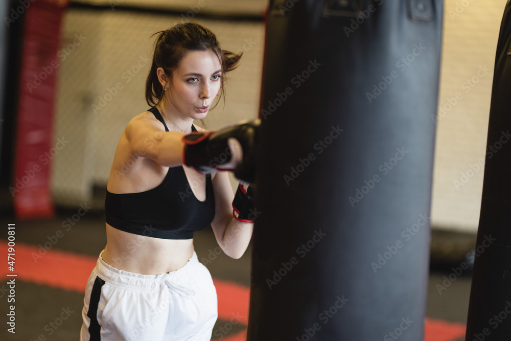 Skinny young woman performs punching bag punches. Women's fitness boxing workout in the gym. 